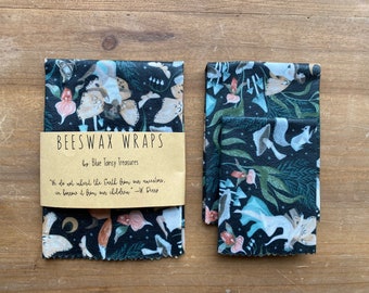 May include: Two sets of beeswax food wraps with a black background and a whimsical pattern of mushrooms, flowers, and moths. The wraps are packaged with a brown paper label that reads "Beeswax Wraps by Blue Tansy Treasures" and a quote about inheriting the Earth from our ancestors.