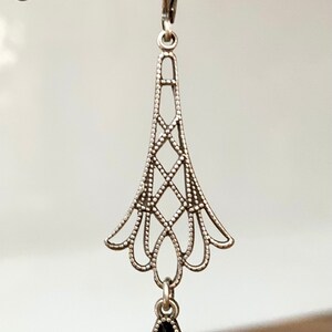 May include: Silver-toned filigree earring with a teardrop-shaped, dark blue gemstone and a small, round, clear stone. The earring has a decorative, openwork design with a lever-back closure. The earring is suspended from a decorative metal fixture.