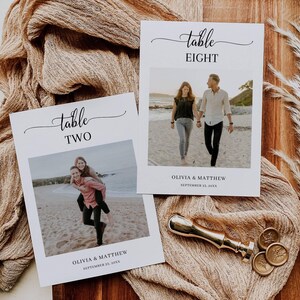 Puede incluir: Dos tarjetas de mesa de boda con fondo blanco y texto negro. La parte superior de cada tarjeta dice "mesa" seguida del número de mesa. Cada tarjeta tiene una foto de una pareja en una playa. El texto debajo de la foto dice "Olivia & Matthew" y la fecha "September 25, 20XX".