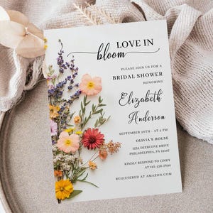 May include: A white bridal shower invitation with a floral design. The invitation reads "Love in Bloom" and includes the bride's name, Elizabeth Anderson, the date and time of the shower, and the location.