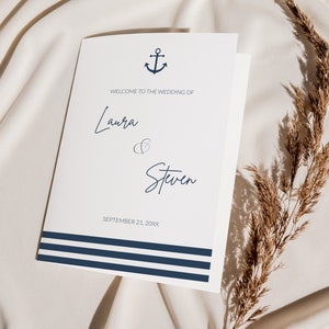 May include: A folded wedding program with a navy blue anchor icon and horizontal stripes. The text reads "Welcome to the Wedding of Laura & Steven, September 21, 20XX". The program is on a cream-colored fabric.