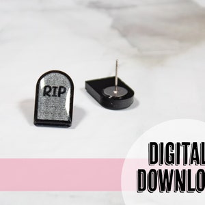 May include: A pair of black and silver earrings shaped like a tombstone with the word "RIP" on the front. The earrings are on a white surface.
