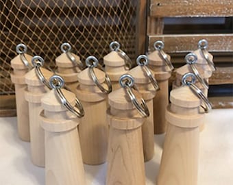 May include: A collection of wooden lighthouse keychains. Each keychain features a natural wood finish, a cylindrical body, a domed top, and a silver-colored keyring. The keychains are arranged in a group, suggesting they are for sale or display.