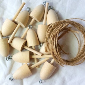 May include: A collection of unfinished wooden buoys with metal eyelets, alongside a coil of natural twine. The buoys have a rounded top and a cylindrical base, perfect for crafting or nautical-themed projects. The light wood color contrasts with the brown twine.