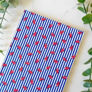 May include: A blue and white striped notebook with a red fish pattern. The notebook has a bright orange bookmark.