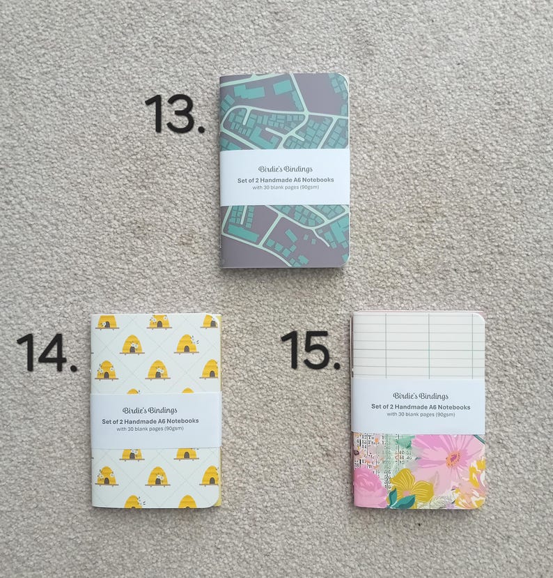 May include: Set of two A6 notebooks with 30 blank pages. The notebooks have different designs: a city map, a beehive pattern, and a floral pattern. Each notebook has the text "Birdie's Bindings" printed on the cover.