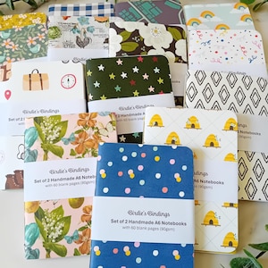 Peut inclure: Un ensemble de 12 carnets A6 faits à la main avec 60 pages vierges. Les carnets ont des couvertures colorées variées avec différents motifs, notamment floraux, géométriques et à pois. Les couvertures sont en papier et ont une finition mate.