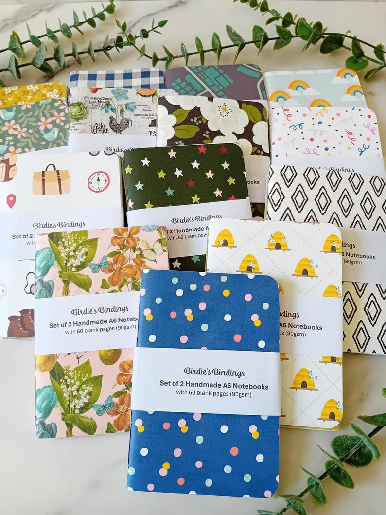 May include: A set of 12 handmade A6 notebooks with 60 blank pages. The notebooks have various colorful covers with different patterns, including floral, geometric, and polka dots. The covers are made of paper and have a matte finish.