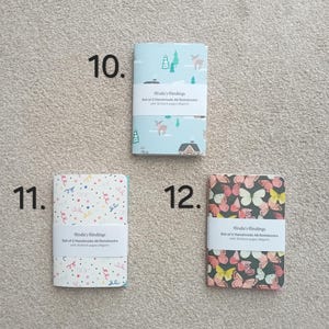 May include: Set of two A6 notebooks with 30 blank pages. The notebooks have different designs: one with a winter scene, one with a confetti pattern, and one with a butterfly pattern.