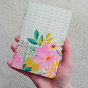 May include: A small, pink and green floral notebook with a grid pattern on the cover.