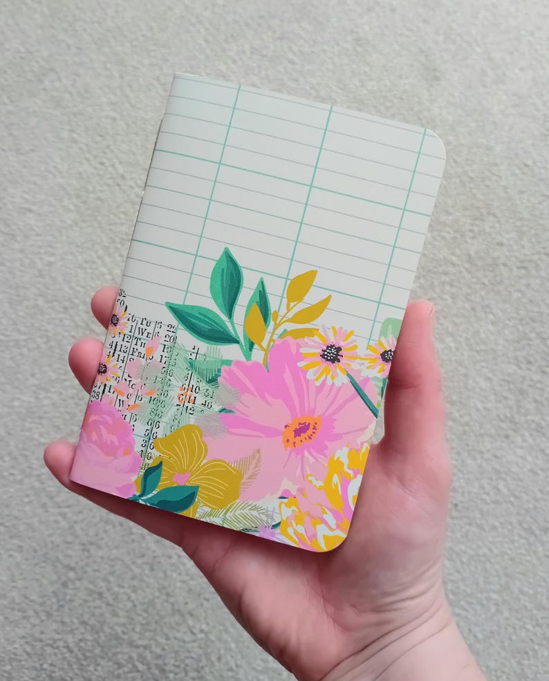 May include: A small, pink and green floral notebook with a grid pattern on the cover.