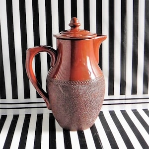 May include: A brown ceramic coffee pot with a lid and a textured surface. The pot has a handle and a spout.