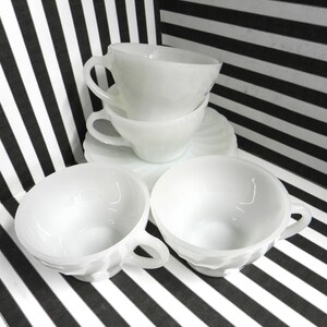 Puede incluir: Cuatro tazas de té de cerámica blanca apiladas sobre un platillo blanco. Las tazas tienen un diseño acanalado y están hechas de cerámica blanca opaca.