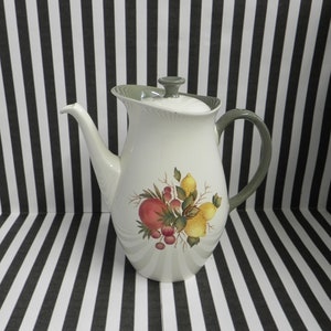 Puede incluir: Una cafetera de cerámica blanca con tapa y asa verdes. La cafetera tiene un diseño floral con limones, manzanas y bayas.