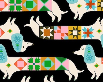 May include: A black fabric featuring a repeating pattern of cream-colored dachshunds with light blue ears and bodies decorated with colorful geometric quilt-style blocks. A ruler at the bottom shows the fabric width in inches, labeled Ruby Star Society.