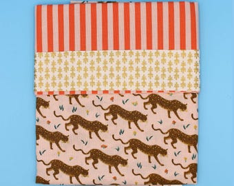 May include: Folded fabric with three distinct patterned sections. The top section features orange and white vertical stripes. The middle section has a gold floral pattern. The bottom section displays a pink background with brown leopard print.