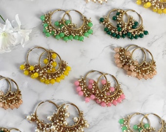 May include: A collection of gold hoop earrings with dangling beads. The earrings feature different colored beads, including green, pink, yellow, and white.