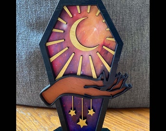 May include: A wooden stand with a black base and a purple, gold, and brown design. The design features a crescent moon, stars, and a hand reaching up towards the moon.