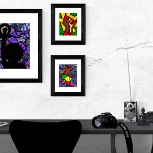 Pu&ograve; includere: Tre stampe d'arte incorniciate con disegni astratti colorati che presentano silhouette nere di persone. Le stampe sono appese a una parete bianca sopra una scrivania nera con una macchina fotografica, una radio e una piccola statua.