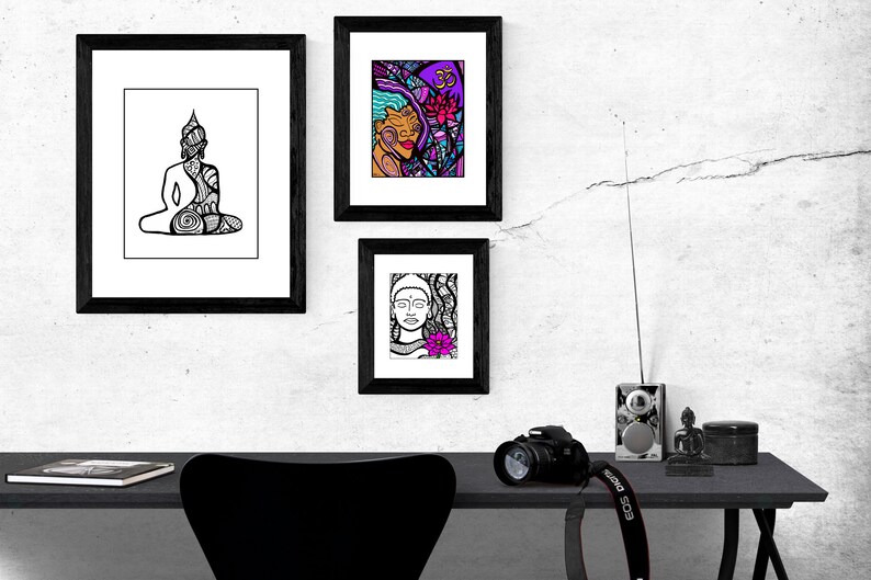 May include: Three black framed prints with white mats hanging on a white wall. The prints feature black and white line drawings of a meditating Buddha, a woman's face with a flower, and a woman's face with a flower and a symbol. A black desk with a black chair, a camera, a radio, and a small Buddha statue are in the foreground.