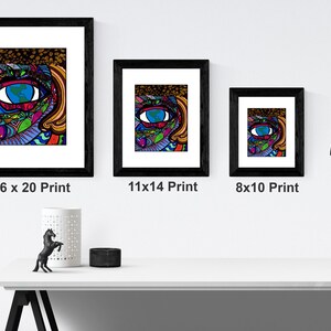 May include: Three framed prints of a colorful, abstract illustration of an eye with a globe inside. The prints are in black frames and are displayed on a white wall. The prints are labeled with their sizes: 16 x 20, 11 x 14, and 8 x 10.