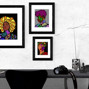 May include: Three framed black and white illustrations of women with colorful patterned clothing and hair. The illustrations are hung on a white wall with a crack running through it. A black desk with a camera, a radio, and a small statue is in the foreground.