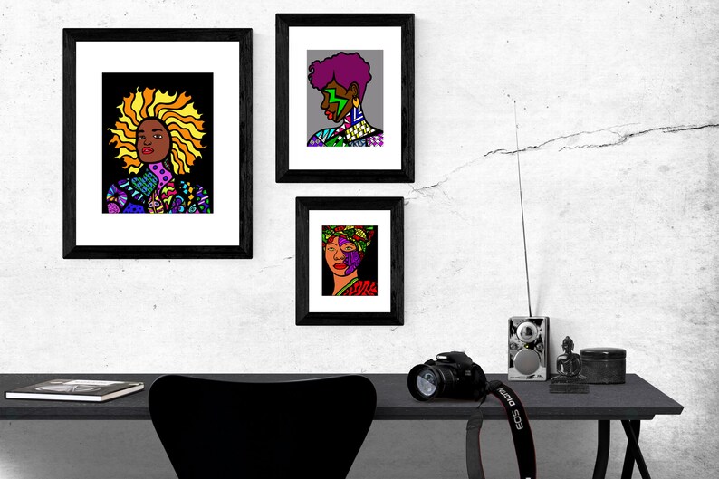 May include: Three framed black and white illustrations of women with colorful patterned clothing and hair. The illustrations are hung on a white wall with a crack running through it. A black desk with a camera, a radio, and a small statue is in the foreground.