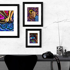 May include: Three framed illustrations with black frames hanging on a white wall. The illustrations are colorful and abstract. The top left illustration features a foot with blue and yellow water droplets. The top right illustration features a couple embracing. The bottom illustration features a colorful eye.