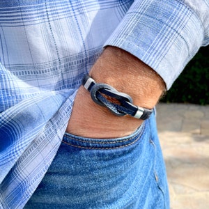 May include: A black leather bracelet with a silver knot design. The bracelet is worn on a person's wrist.