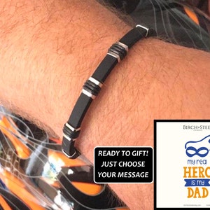 May include: Black silicone bracelet with silver accents. The bracelet is ready to be personalized with a message. The text on the card reads "my real HERO is my DAD".