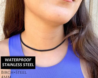 May include: A black chain choker necklace made of waterproof stainless steel. The necklace is 4mm wide and has a black IP finish. The text "WATERPROOF STAINLESS STEEL" is written in white on a black rectangle. The text "BIRCH+STEEL" is written in white on a black rectangle. The text "4MM" is written in white on a black rectangle. The text "BLACK IP STAINLESS STEEL" is written in white on a black rectangle.