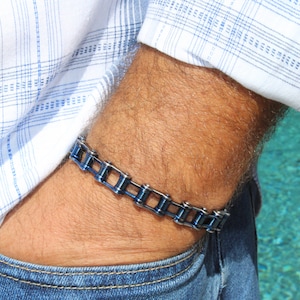 May include: A silver chain bracelet with a blue finish. The bracelet is made of metal links that resemble a bicycle chain.