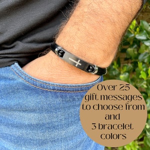 May include: A black leather bracelet with a silver cross charm. The bracelet is shown on a person's wrist. Over 25 gift messages to choose from and 3 bracelet colors.