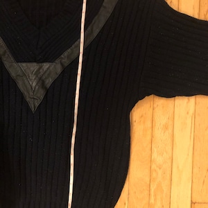May include: A navy blue ribbed knit sweater with a V-neckline and a black leather V-shaped chest accent. A white measuring tape is placed vertically over the sweater, showing a length of approximately 28 inches from the shoulder to the hem.