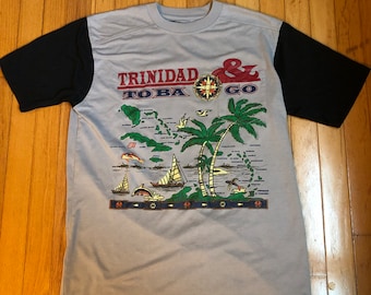 May include: A gray t-shirt with a black and white design featuring a map of Trinidad and Tobago with palm trees, sailboats, and fish. The text "Trinidad & Tobago" is printed on the shirt.