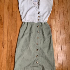 Könnte beinhalten: Ein zweiteiliges Vintage-Kleid mit cremefarbenem Oberteil und salbeigrünem Rock. Das Kleid hat einen V-Ausschnitt, kurze Ärmel und eine Reihe brauner Knöpfe auf der Vorderseite. Das Kleid ist aus einem leinenartigen Stoff gefertigt.