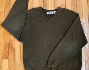 May include: A dark green v-neck sweater with long sleeves and a ribbed hem. The sweater has a small logo on the front that says "Northwest Territory".