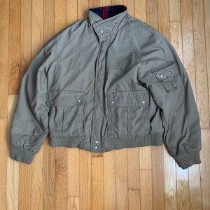 May include: A tan, quilted jacket with a zipper closure and a plaid lining. The jacket has multiple pockets and a ribbed hem and cuffs.