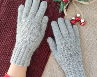 Puede incluir: Un par de guantes de punto grises con un patrón texturizado. Los guantes están sobre un fondo marrón y rojo.