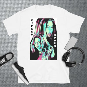 May include: White t-shirt featuring a graphic print of three women in a neon green and pink colour scheme. The text "Ginger Snaps" is printed vertically on the right side of the graphic.