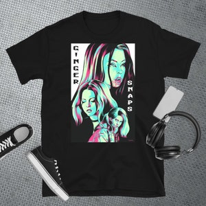 May include: Black t-shirt featuring a graphic print of three women with pink and blue accents. The text "Ginger Snaps" is printed vertically on the left side of the graphic.