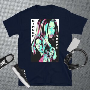 May include: A navy blue t-shirt featuring a graphic print of three women with pink and blue accents. The text "Ginger Snaps" is printed vertically on the right side of the graphic.