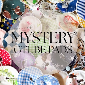 May include: A collection of colorful, circular G-tube pads with various patterns, including polka dots, gingham, and sports-themed designs. The pads are made of fabric and feature a central opening. The text "MYSTERY GTUBE PADS" is overlaid on the image.