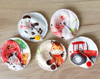 May include: Set of five round, white fabric pads with farm animal and tractor designs. Each pad features a different illustration: a cow, pig, horse, tractor, and a cow with a barn. The pads have a button closure.
