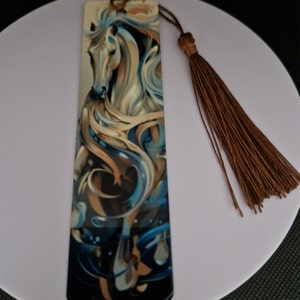 K&ouml;nnte beinhalten: Rechteckiger Lesezeichen mit einem k&uuml;nstlerischen Bild eines wei&szlig;en Pferdes mit flie&szlig;ender M&auml;hne und Schweif, in Blau-, Gold- und Braunt&ouml;nen. Ein brauner Quastenanh&auml;nger ist befestigt. Ideal zum Markieren von Seiten in B&uuml;chern.