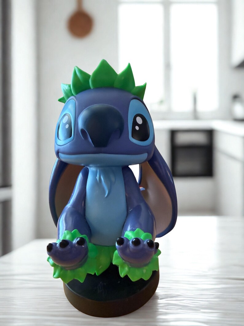 Puede incluir: Una figura azul y verde del personaje Stitch de la pel&iacute;cula de Disney Lilo & Stitch. La figura tiene orejas grandes, una nariz grande y detalles verdes en la cabeza y los pies. La figura est&aacute; sobre una base marr&oacute;n.