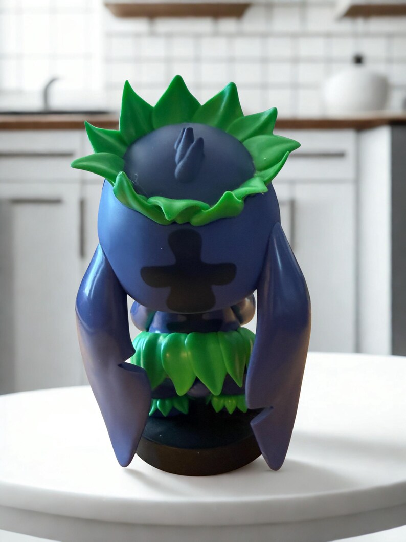 Puede incluir: Figura azul y verde con un dise&ntilde;o &uacute;nico. La figura tiene una cabeza redonda con detalles verdes en forma de hojas y un dise&ntilde;o negro en forma de cruz en la parte delantera. Est&aacute; sobre una superficie blanca.