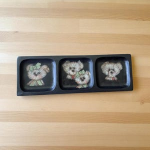 May include: A rectangular black serving tray with three compartments. Each compartment features a different illustration of a teddy bear with a bow. The bears have tan fur and are wearing bows in shades of green and red.