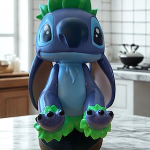 Puede incluir: Figura de Stitch azul y verde. La figura tiene ojos negros grandes, una nariz grande y detalles verdes en la cabeza y los pies. La figura est&aacute; sobre una base marr&oacute;n.