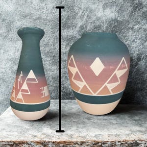 May include: Two ceramic vases with geometric patterns in teal, peach, and cream. The taller vase has a narrow neck and a geometric design. The shorter vase is rounder with a similar design. The vases are displayed on a stone surface.